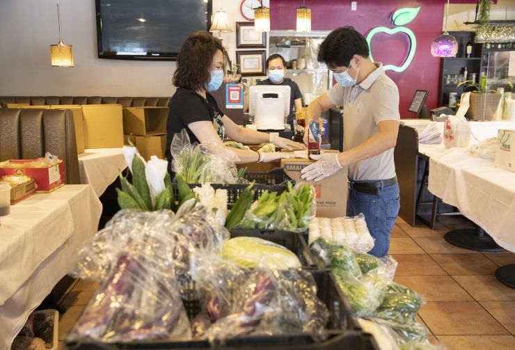 当地时间5月9日，在硅谷腹地库比蒂诺商圈的“青苹果”餐馆，店主汪女士（左）与合伙人将不同类型的物资装进纸箱，并用胶带封好。之后，这些物资将被送往客户手中。新冠肺炎疫情暴发后，餐馆开始为客户提供采购生活物资的服务。（图片来源 中新社）