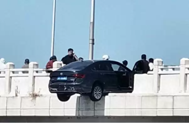 轿车撞断大桥护栏悬空中 过路男子冲上前压住车头
